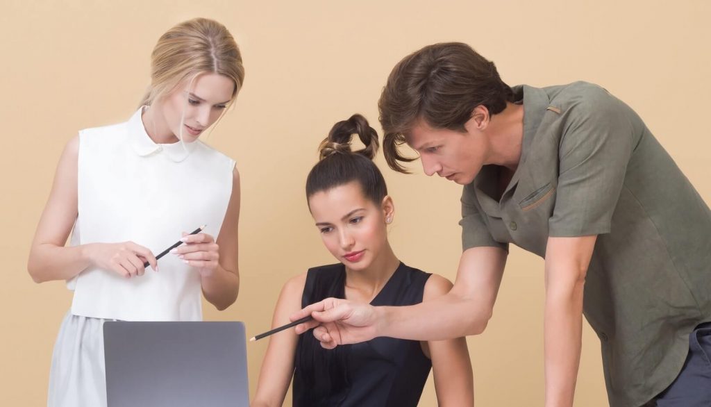 Duas mulheres e um homem conversam apontando para computador